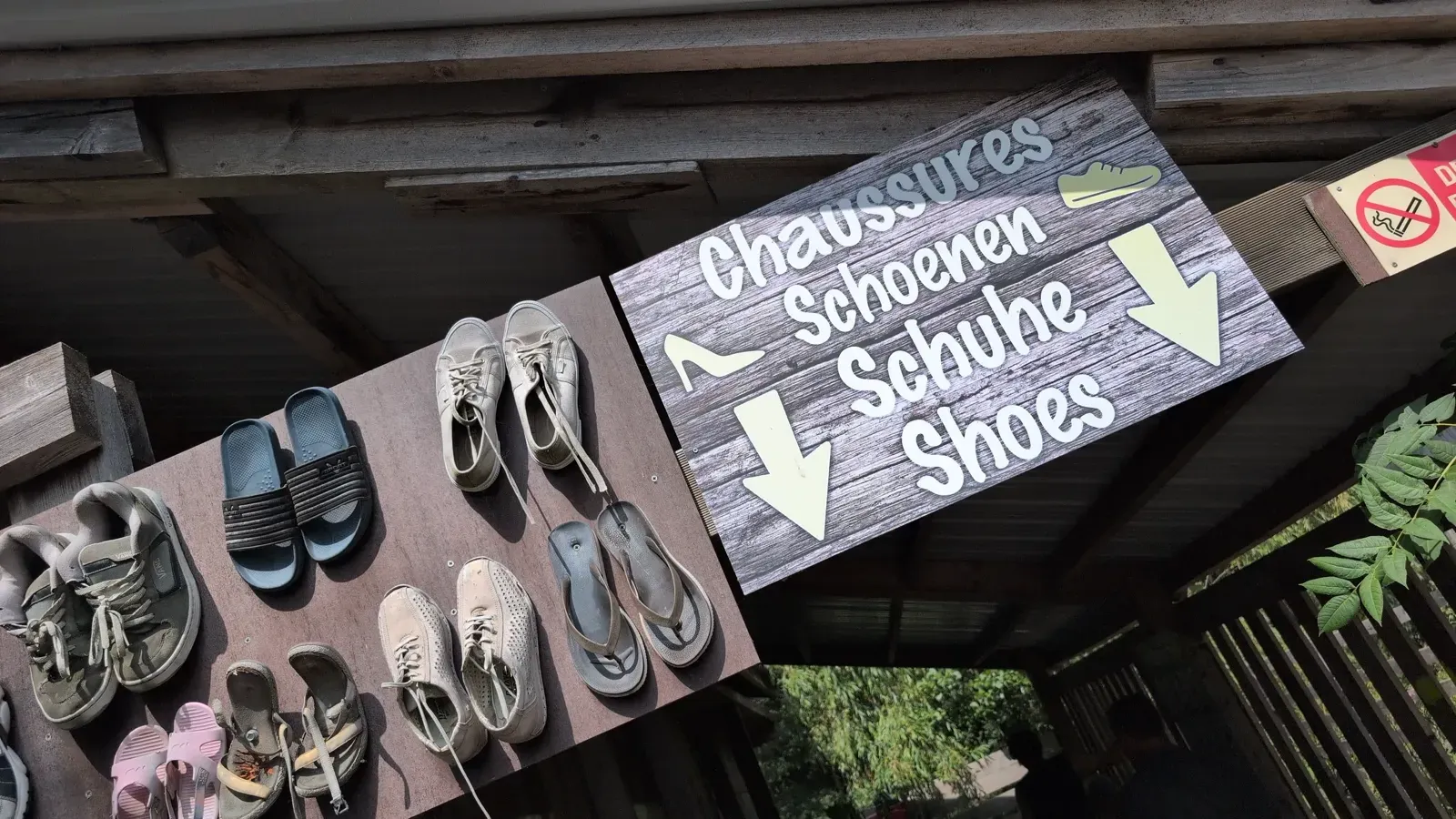 Multilingual sign inviting visitors to leave their shoes before the barefoot trail